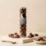chocolate-covered-raisins A 300x300 square professional flat-lay photograph featuring a single, perfect square of Tennessee Whiskey milk chocolate. The chocolate has a rich, glossy brown finish and is perfectly centered on a light cream-colored linen napkin with visible hemstitch detailing. The aesthetic is clean and minimalist, with soft, even lighting that emphasizes the silky texture of the chocolate against the natural weave of the fabric. The composition is balanced and elegant, focusing entirely on the simple, indulgent quality of the chocolate.